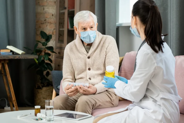 hombre mayor mascara protectora sosteniendo recipiente pastillas mirando joven doctora bata blanca recetandole nuevo medicamento